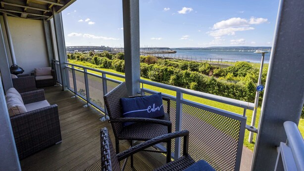 A covered balcony with wicker furniture and a view of the sea and a bridge.