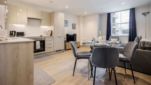 Une cuisine moderne dotée d’appareils électroménagers intégrés, un coin repas avec une table en verre et un espace de vie comprenant un canapé et un téléviseur.
