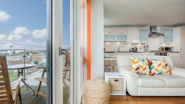 Un appartement moderne doté d’un balcon, d’une cuisine et d’un espace de vie comprenant un canapé et des coussins aux couleurs vives.