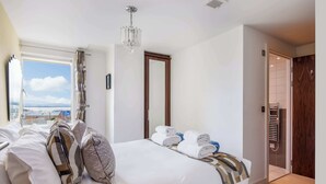 Une chambre d’hôtel avec un grand lit, une vue sur la ville, un lustre et une porte en bois.