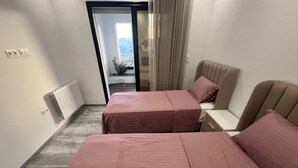 A bedroom with two beds, a radiator, a window, and a view of the outside. - Superb Apartment S+2 Sahloul 4 Sousse (Sousse)