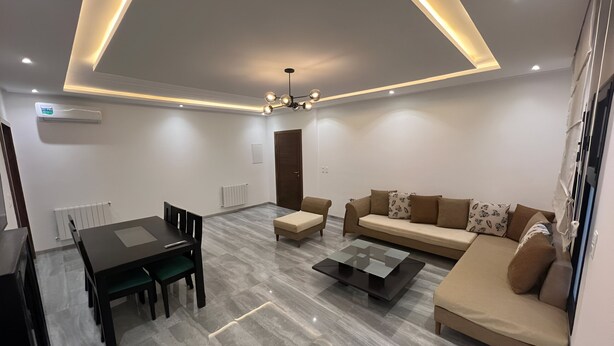 A modern living room with a sofa, coffee table, and dining area. - Superb Apartment S+2 Sahloul 4 Sousse (Sousse)