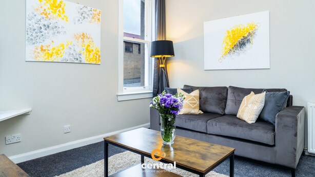 A living room with a grey sofa, a coffee table, and two abstract paintings on the wall.