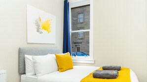 A hotel room with a bed, a window with a view of a building, and a painting on the wall.