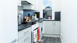 A compact kitchen with white cabinets, a built-in oven, a washing machine, and a window providing a view of the outside.