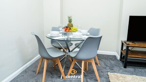 A dining area with a glass table, grey chairs, and a fruit bowl.