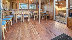 Een houten hutje van binnen met een eethoek, een badkamer en een raam met uitzicht op bomen.
