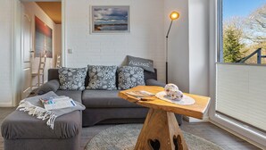 Een moderne woonkamer met een grijze bank, een houten salontafel en een groot raam met jaloezieën.