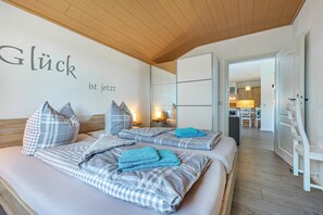 Ein Hotelzimmer mit zwei Betten, karierten Bettbezügen, einer Holzbalkendecke und einer Wand mit einem deutschen Spruch.
