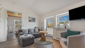 Een moderne woonkamer met een grijze bank, een ronde houten salontafel en een grijze fauteuil.