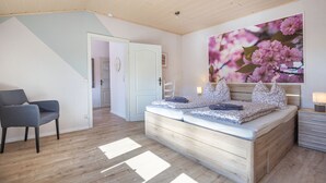 A bedroom with a bed, a chair, a door, and a large floral painting on the wall.