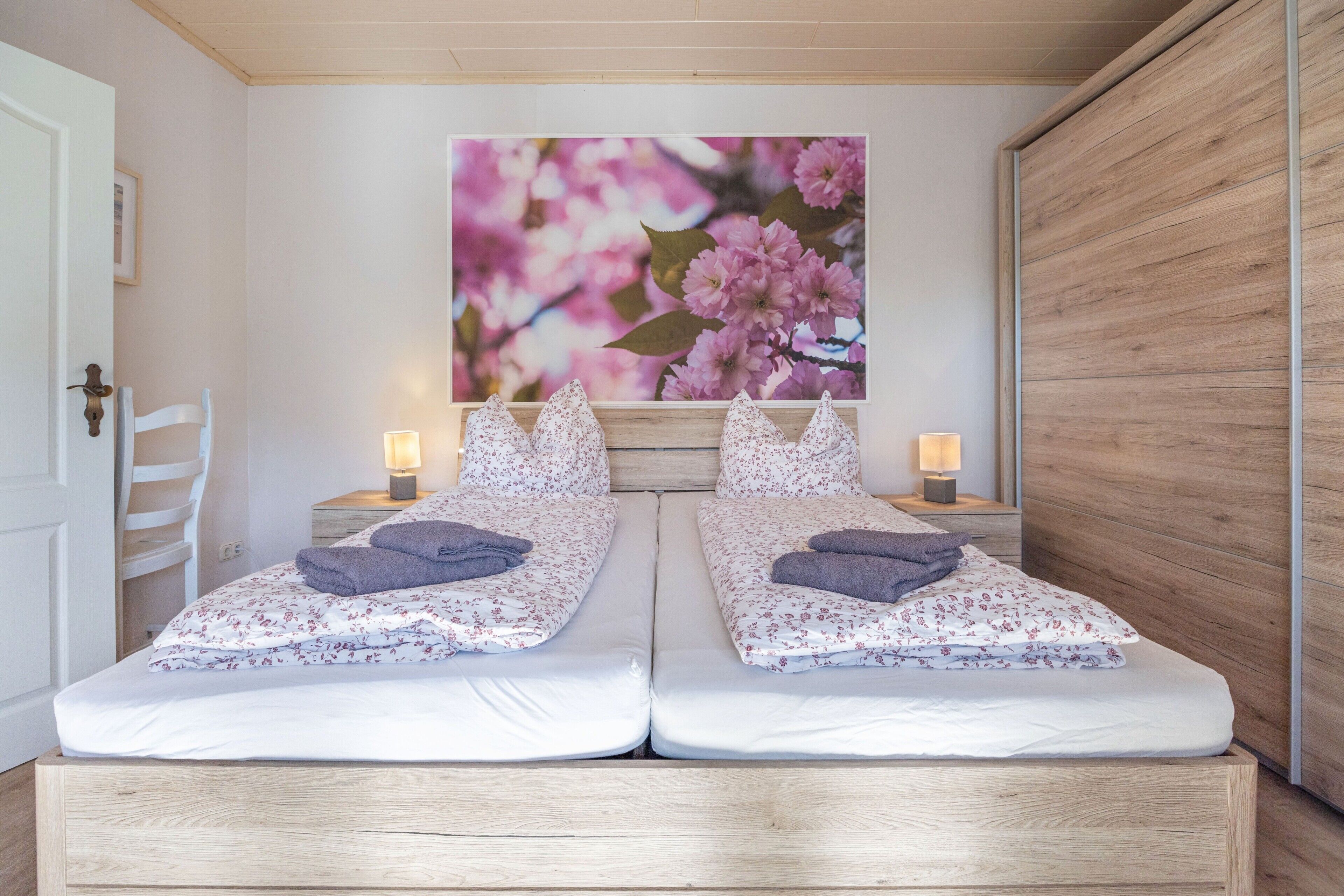 A double bed with floral bedding, two bedside lamps, and a large floral painting on the wall.
