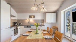A modern kitchen with white cabinets, a wooden dining table, and a large window.