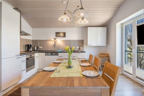 Une cuisine moderne avec des meubles blancs, une table à manger en bois et une grande fenêtre.