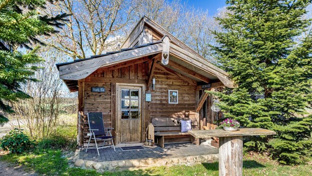 A rustic cabin with a wooden exterior, a porch with a bench, and a small table with a flower pot.