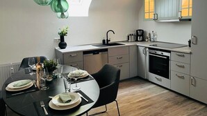 Moderni keittiö, jossa on ruokailutila, ja jossa on muun muassa kattovalokuvio, ruostumattomasta teräksestä valmistetut kodinkoneet ja minimalistinen muotoilu.