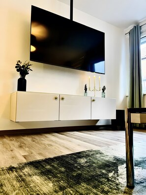 A modern living room with a mounted TV, a white cabinet with decorative items, a wooden floor, and a dark green rug. - Apartment 'Ferienwohnung Stern' with Shared Terrace and Wi-Fi (Goslar)