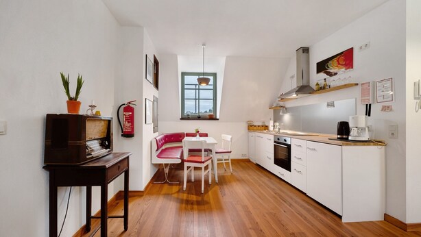 Een compacte keuken met een eethoek, houten vloeren, witte kastjes en een kleine tafel met stoelen.