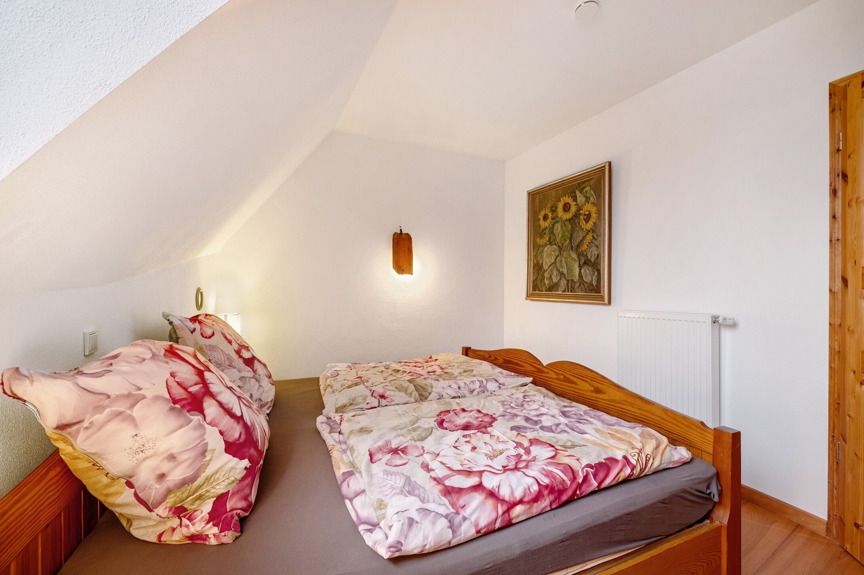 A bedroom with a wooden bed, a wall-mounted light, and a painting.