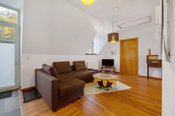 Una sala de estar con un sofá seccional, una mesa de centro de vidrio, un televisor y una puerta de madera.