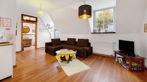 Een moderne woonkamer met een bruine bank, een ronde salontafel, een televisie op een houten dressoir en een groot raam met uitzicht op bomen.