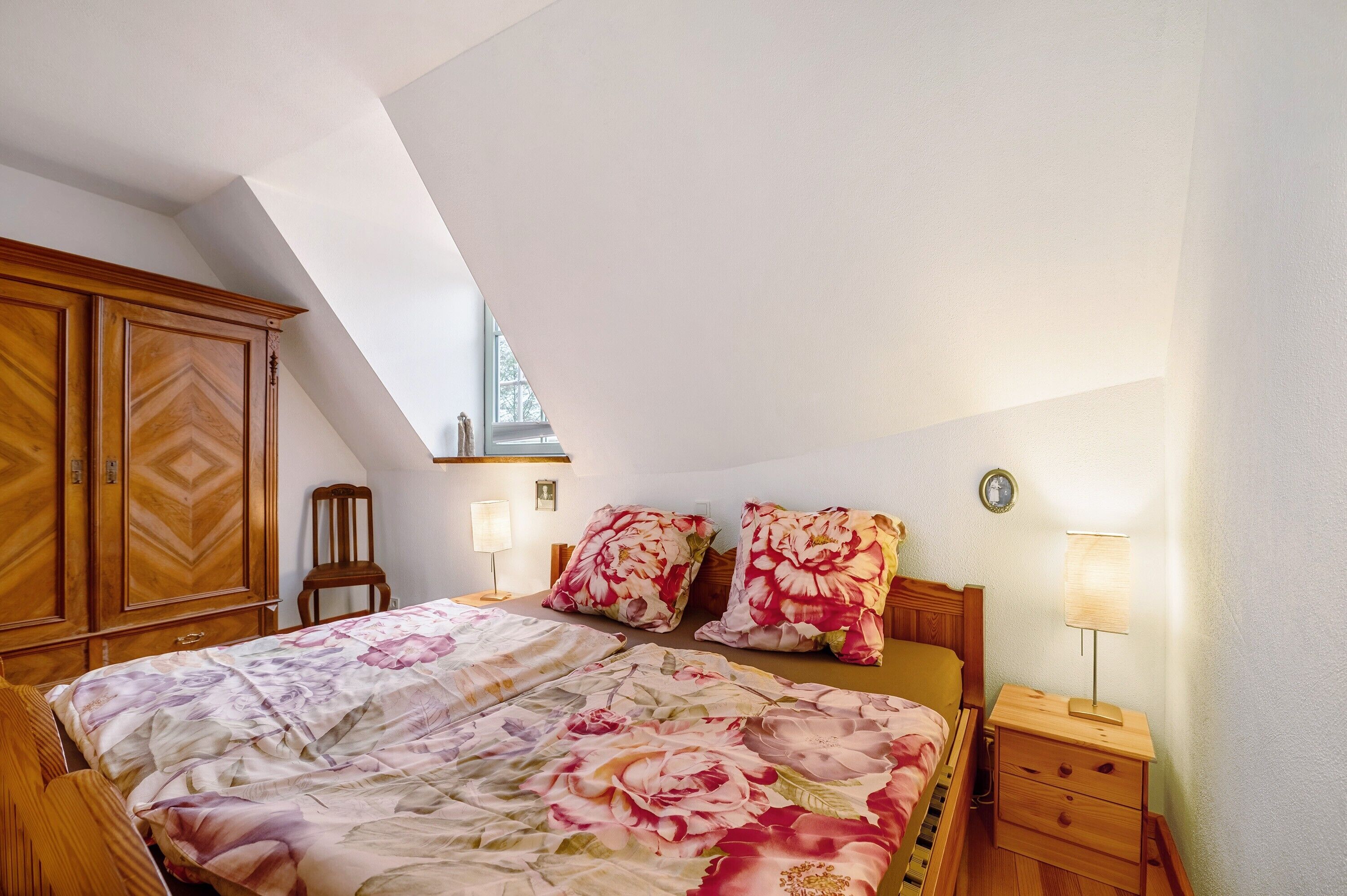 A bedroom with a bed, wooden wardrobe, nightstands, lamps, and a window.