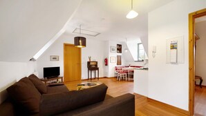 Een woonkamer met een bank, een televisie, een eettafel met stoelen, een keukenhoek en een houten deur.