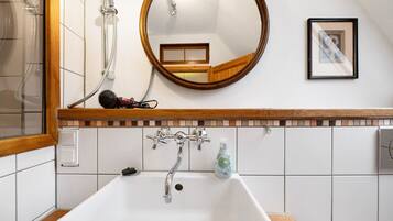 Un baño con lavamanos blanco, tocador de madera, espejo y ducha.