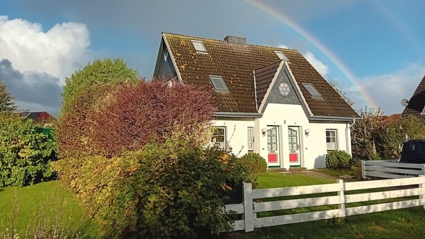 Ein Haus mit geneigtem Dach, weißem Zaun und einem Regenbogen am Himmel.