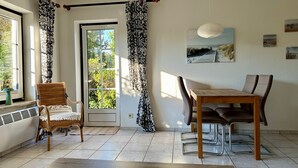 Ein Zimmer mit Esstisch, Stühlen, einem Fenster mit Vorhängen, einem Heizkörper und einer Tür.