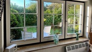Ein Zimmer mit einem großen Fenster mit Blick auf einen Garten, einem weißen Heizkörper und einem kleinen Tisch mit einer Vase.