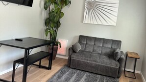 Olohuoneessa on harmaa sohva, musta sohvapöytä, harmaa matto, ruukussa oleva viherkasvi ja seinälle asennettu televisio.