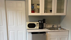 Kompakti keittiö, jossa on valkoiset kaapit, mikroaaltouuni, kahvinkeitin ja pieni jääkaappi.