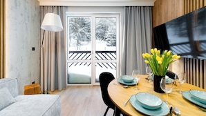 Un comedor con una mesa de madera dispuesta para dos personas, un jarrón con tulipanes amarillos y un televisor de pantalla plana grande montado en la pared.