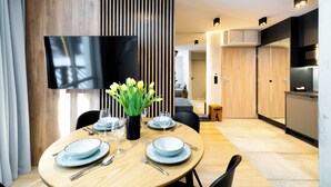 Un comedor moderno con una mesa redonda para dos personas, un televisor de pantalla plana en la pared y un separador de madera con listones verticales.