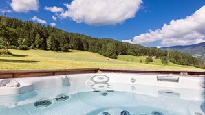 A hot tub with a clear view of a lush green landscape and a mountain range in the background. - Modern chalet with infrared sauna (Sankt Georgen am Kresichberg)