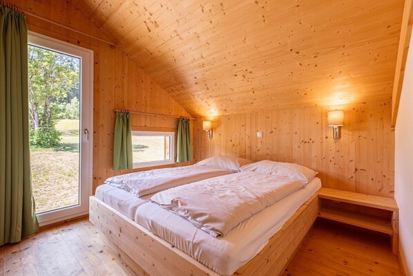 Una habitación de cabaña de madera con dos camas, una ventana con cortinas y un banco.