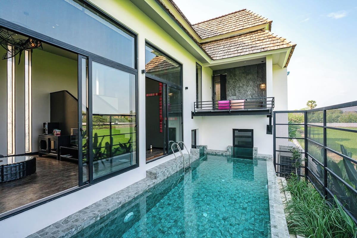 Ein modernes Haus mit einem überdachten Pool, einem Balkon und Blick auf eine grüne Landschaft.