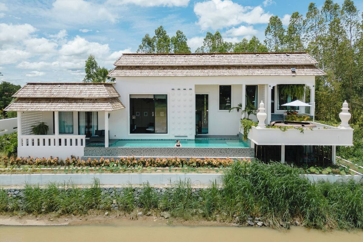 Ein zweistöckiges Haus mit Swimmingpool, überdachter Terrasse und Garten mit Seerosen.