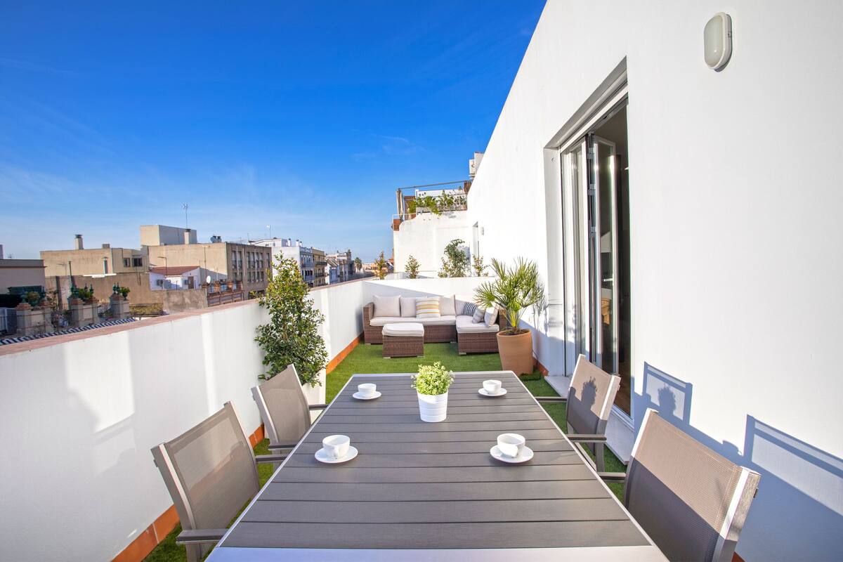 Une terrasse sur le toit avec une table à manger, des chaises et un petit espace aménagé en jardin.