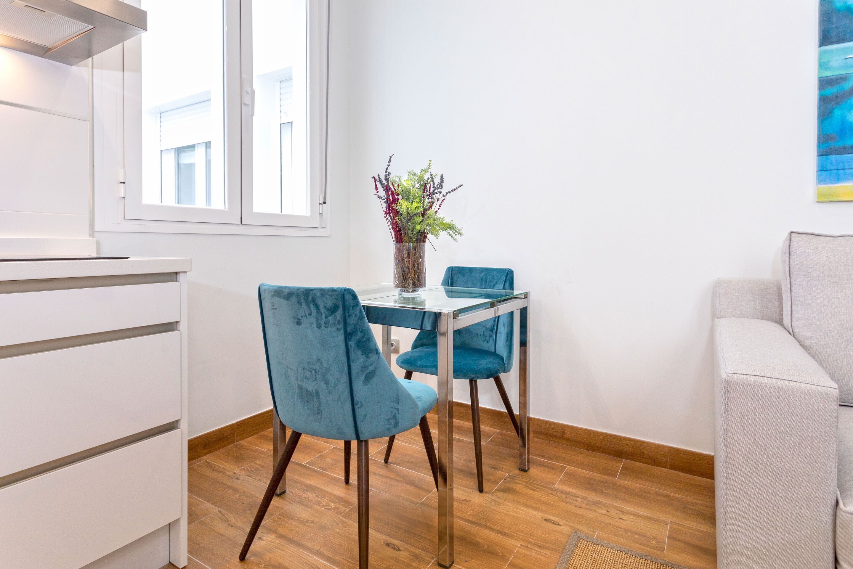 Une pièce moderne comprenant une table à manger, deux chaises, un vase avec des fleurs, un canapé et une fenêtre.