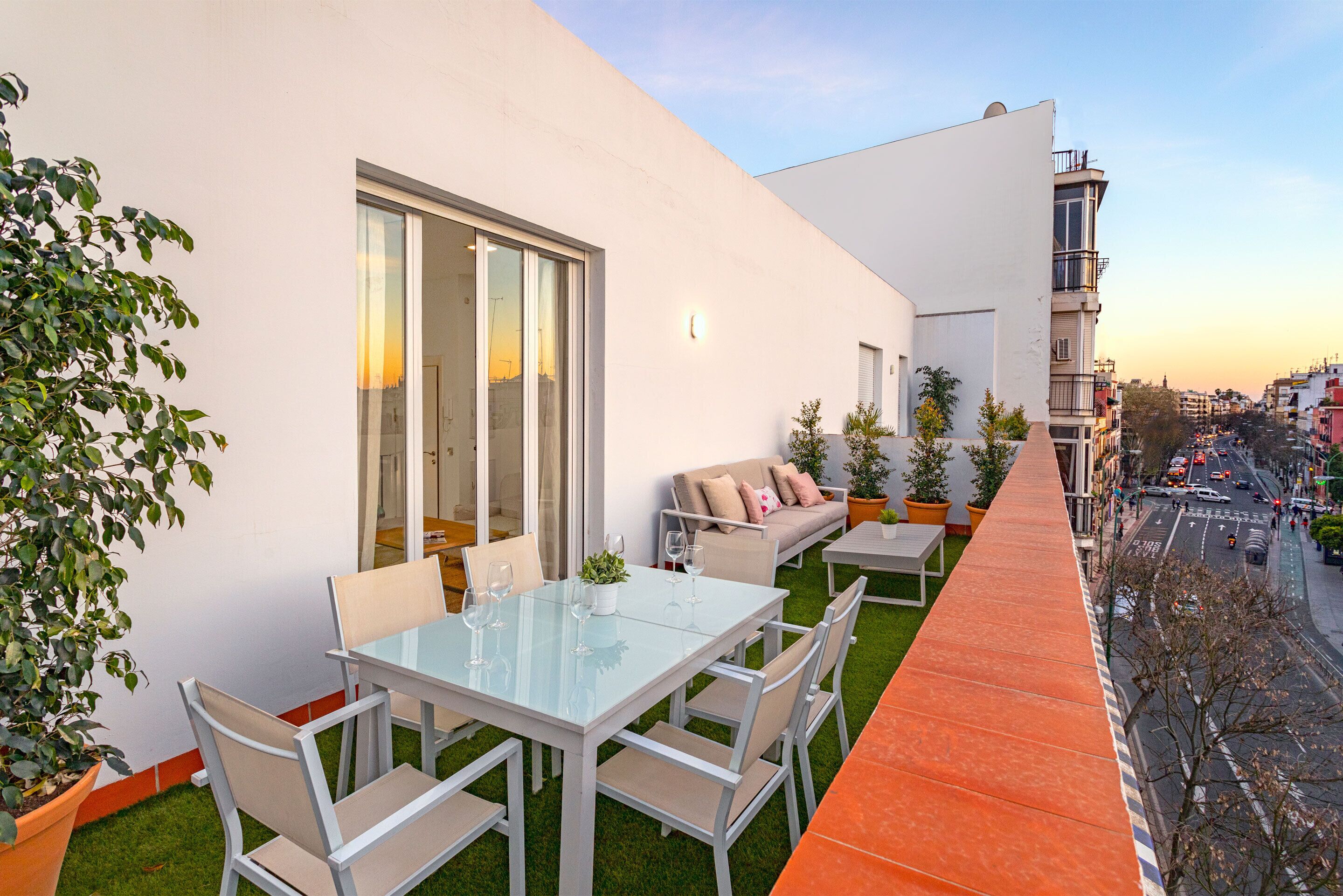 Un patio extérieur moderne avec une table et des chaises en verre, un canapé et des plantes en pot.