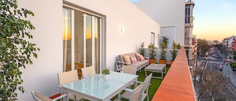 Un patio extérieur moderne avec une table et des chaises en verre, un canapé et des plantes en pot.