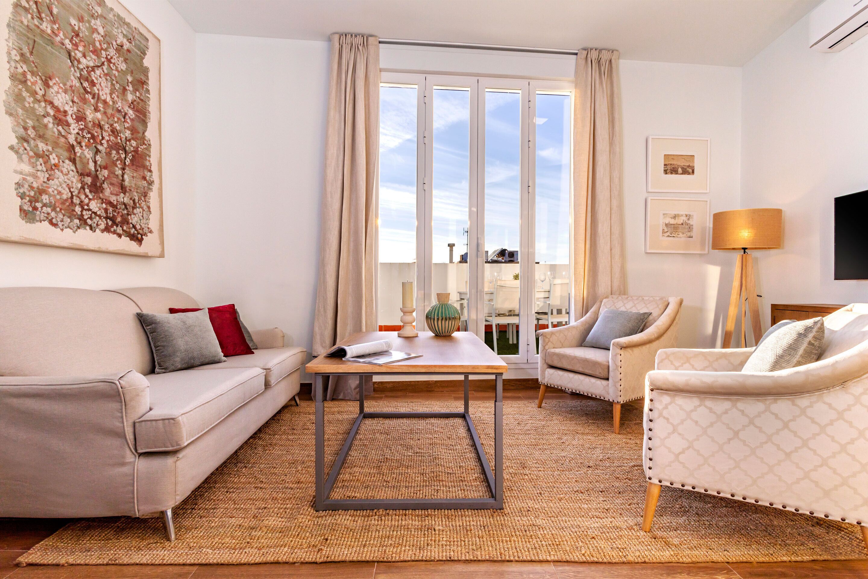 Ein modernes Wohnzimmer mit einer Couch, Sesseln, einem Couchtisch und einem großen Fenster mit Vorhängen.