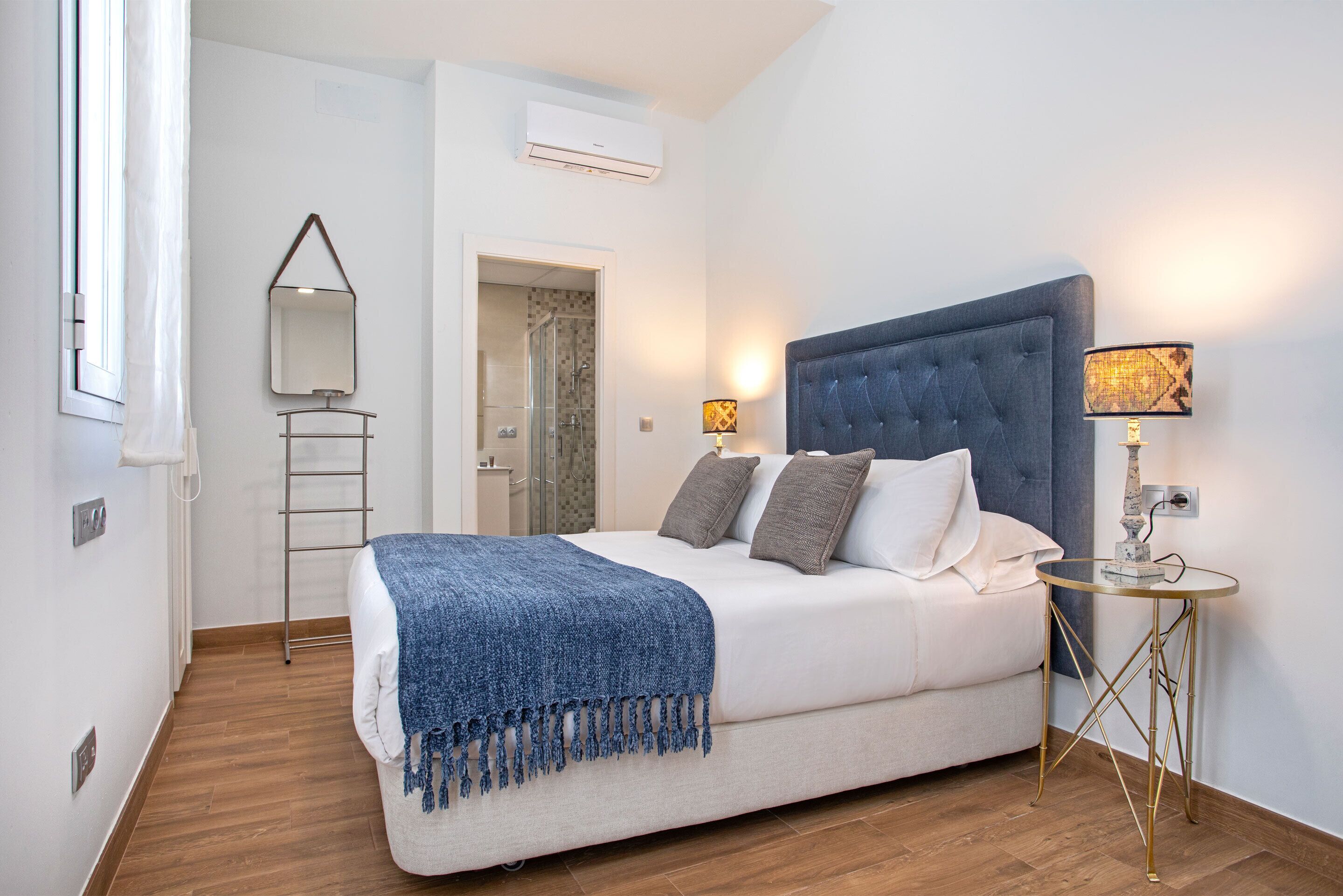 A bedroom with a bed, bedside lamps, a mirror, and a window.