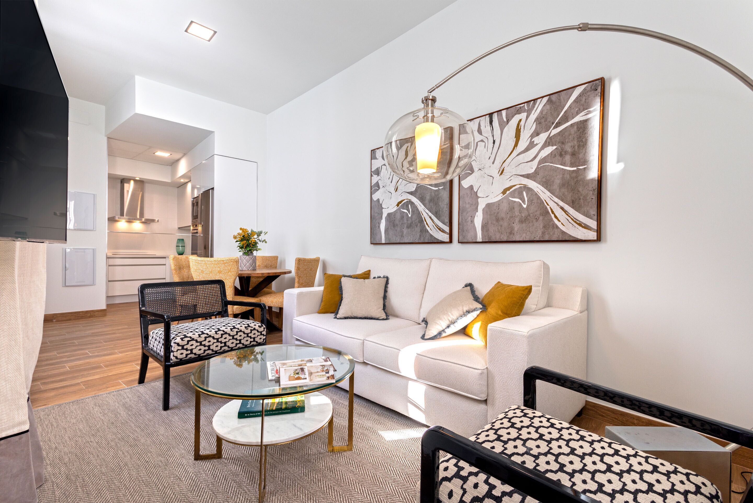 Una sala de estar moderna con un sofá blanco, sillones estampados, una mesa de centro de vidrio y arte abstracto en la pared.