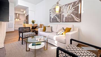 Una sala de estar moderna con un sofá blanco, sillones estampados, una mesa de centro de vidrio y arte abstracto en la pared.