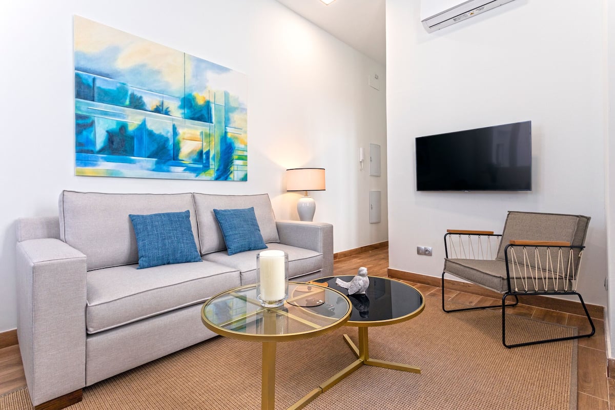 Un salon moderne comprenant un canapé, une table basse en verre, un fauteuil, un tableau, une lampe et un téléviseur.
