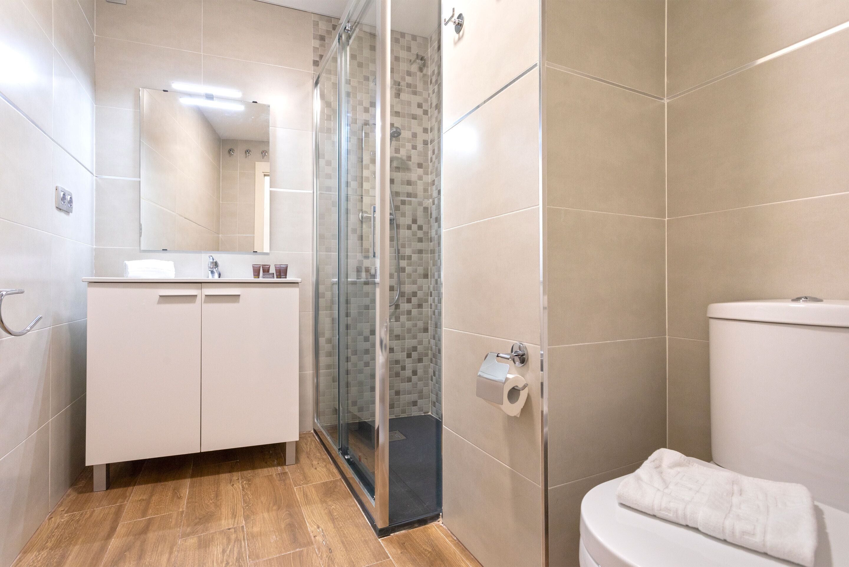 Une salle de bain moderne avec une douche à parois de verre, des toilettes blanches et un meuble-lavabo avec un miroir.