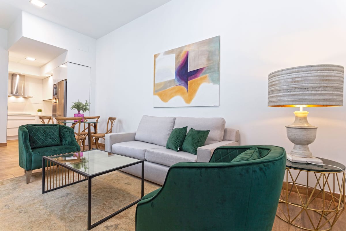 Un salon moderne avec un canapé, deux fauteuils verts, une table basse en verre et une lampe.
